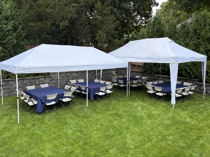 Two white tents with tables, folding chairs, and optional navy tablecloths in a green backyard