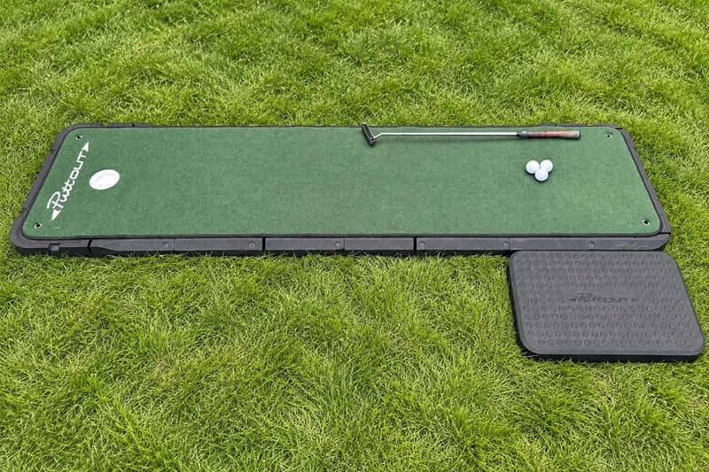 Close view of the putting mat, standing pad, putter, and golf balls